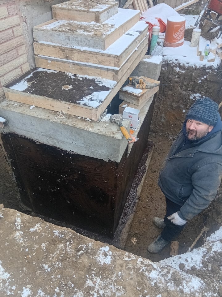 Man standing next to stacked wooden composting bins with soil and snow in a winter garden setting