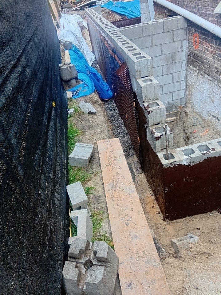 Overhead view of a narrow alley between buildings with concrete blocks, blue tarps, and construction materials on the ground